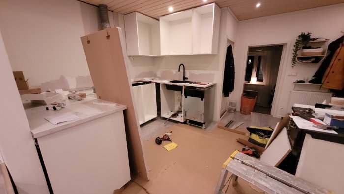 Kök under renovering med omonterade skåpsstommar och verktyg på golvet.