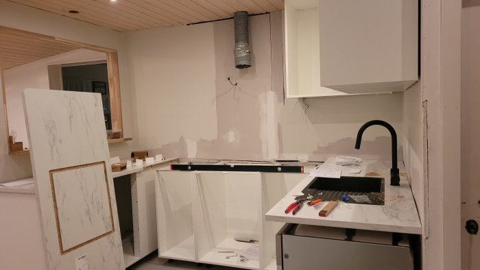 Kök under renovering med omonterade skåpluckor och verktyg på bänkskivan.