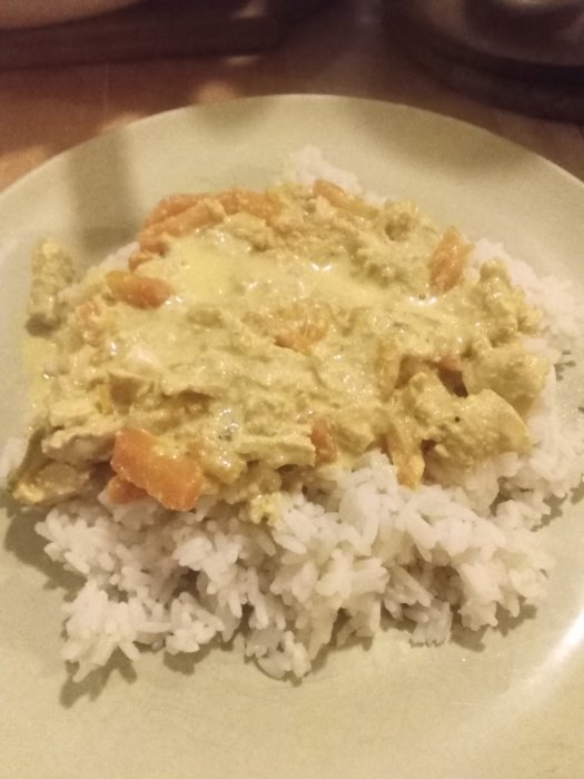 En tallrik med kycklingcurry ovanpå vitt ris, kryddstark och gulaktig i färgen.