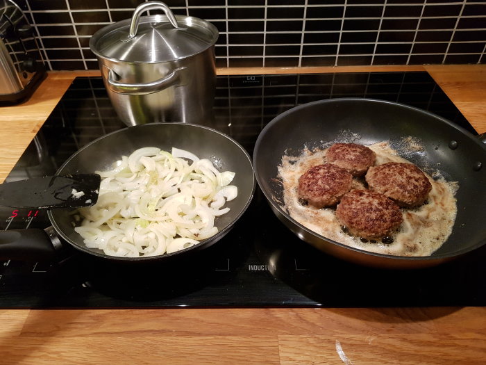 Stekta pannbiffar och lök i två stekpannor på en induktionshäll.