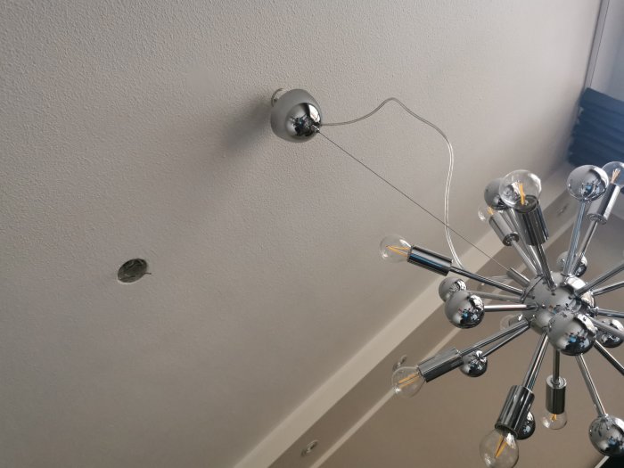 Modernt takmonterat sputnik-ljuskrona med kromade armar och klar glödlampor, med oavslutad installationsdel i taket.