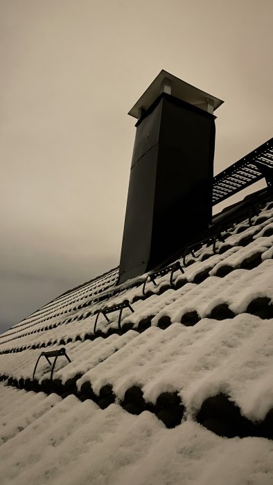 Bild av en skorsten på ett snötäckt tak i skymningen.