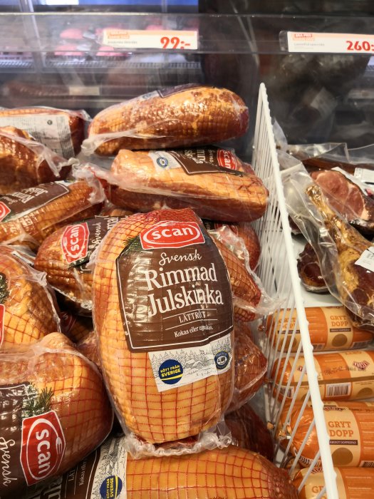 Rimmad julskinka i förpackning framför andra köttprodukter i butikskyl.
