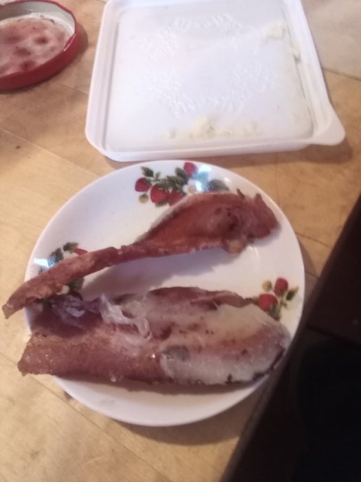 Stekt fläsk på hårdbröd på en vit dekorerad tallrik, tom smörask syns i bakgrunden.