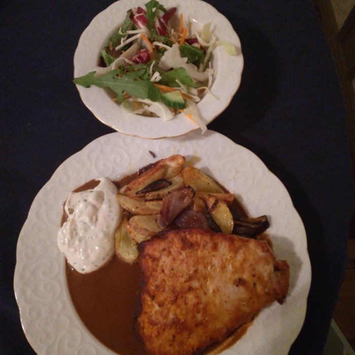 Tallrik med klyftpotatis, fläsknoisette och skysås, samt en salladstallrik.