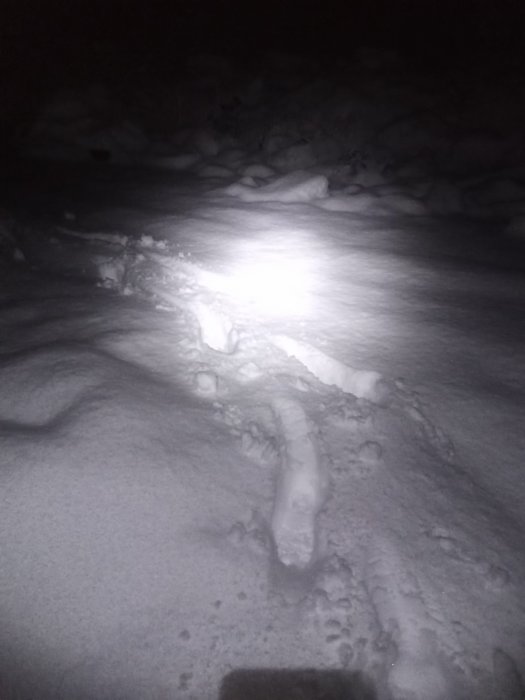 Snöig terräng på natten med spår och fotavtryck i snön.