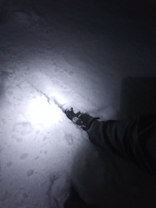 Person som vadar genom djup snö i mörker med en stark ljuskälla i närheten.