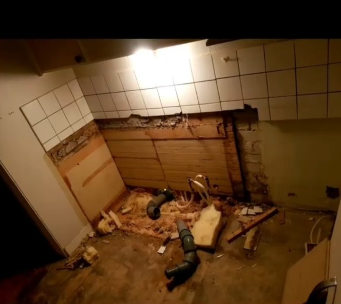 Renoveringsprojekt av badrum med riven kakelvägg och borttaget golv som visar rör och spillror.
