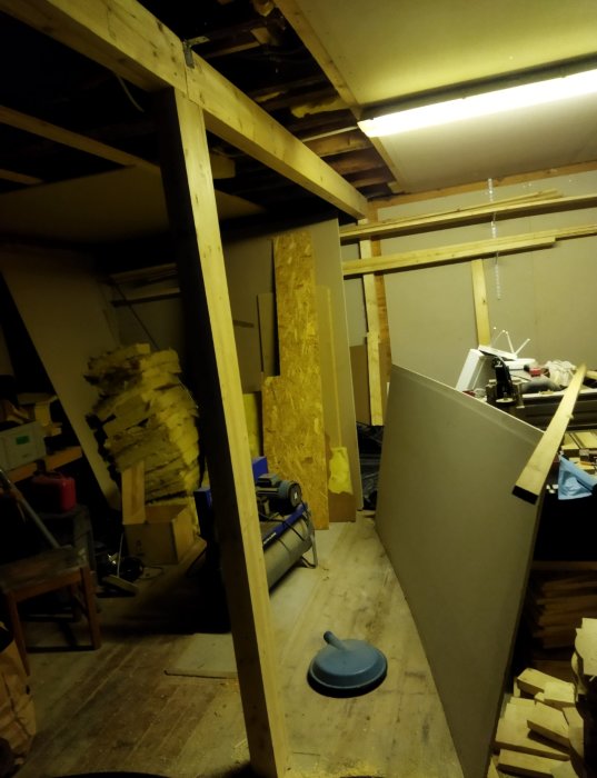 Renoveringsprojekt visar träbjälkar och isoleringsmaterial i ett rörigt källarutrymme.
