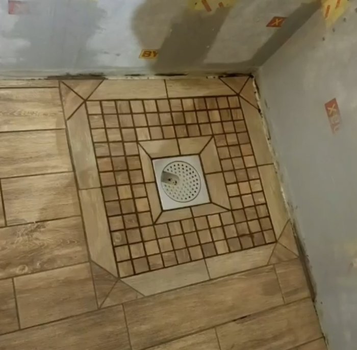 Duschkabinens golv med kakel som möter träimitation klinker, hörnvis med brunn i mitten.