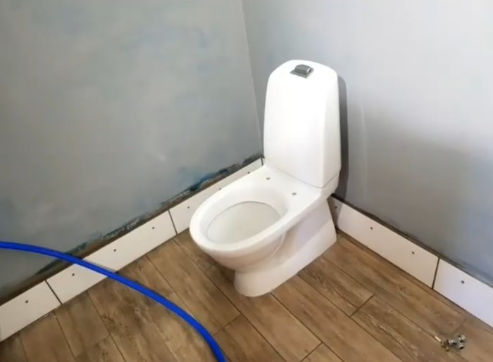 Renoverat badrum med installerad toalett, oskyddade rördragningar och delvis klart golv.