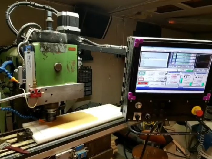 CNC-maskin bearbetar material med datorskärm som visar programmeringsgränssnittet.