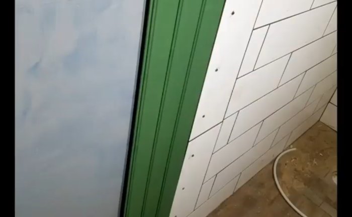 Renoverat badrum med nya vita kakelplattor på vägg och grön tätskiktsmatta vid duschutrymme.