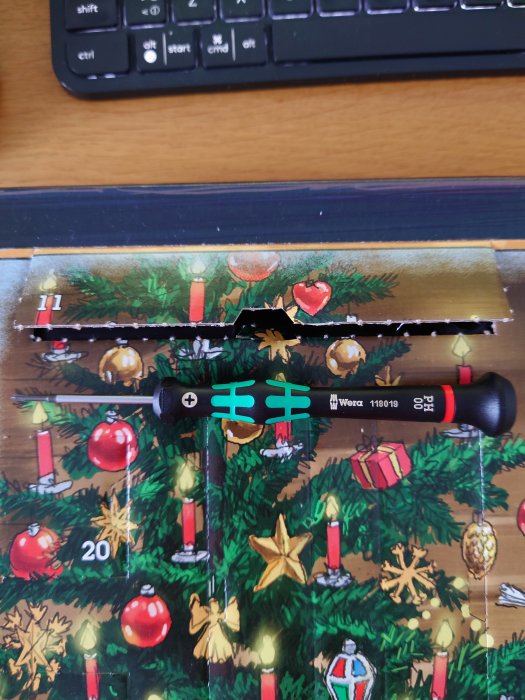 Öppnad lucka på en adventskalender med verktygstema som visar en skruvmejsel framför en julgran med dekorationer.