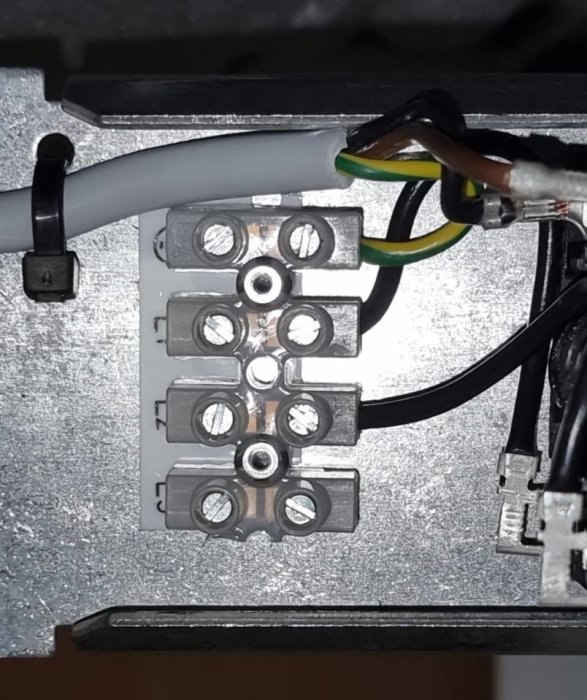 Närbild av en elektrisk anslutning med kablar och skruvklämmor inuti en apparat.