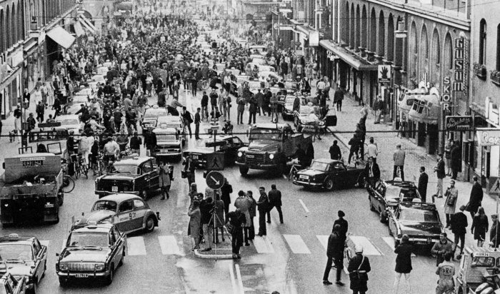 Svartvit bild av en trafikomställning med bilar och människor som korsar gatan.