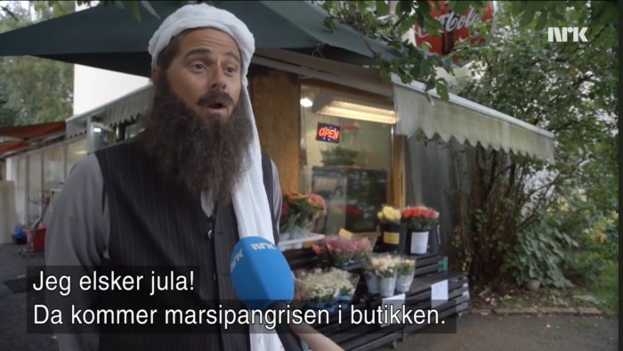 Man iklädd vit turban och skägg intervjuas av NRK med en blomsteraffär i bakgrunden.