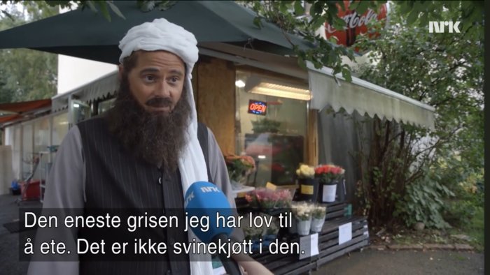 Man med turban intervjuas framför blomsterbutik med skylt som säger "ÖPPET".