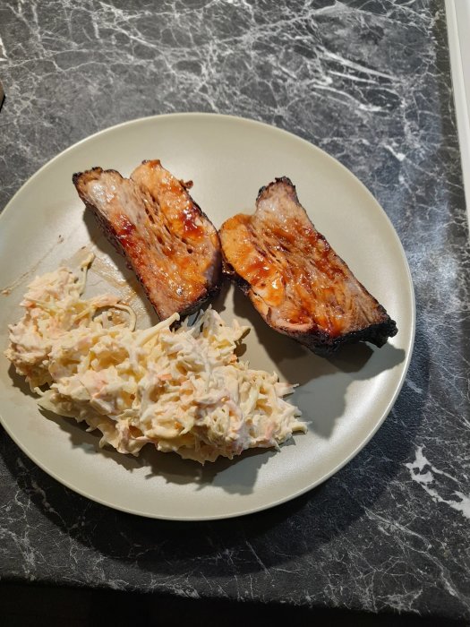 Två stycken ugnsgrillade revbensspjäll och coleslaw på en tallrik.