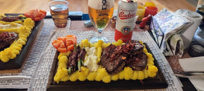 En planka med biff, bacon, pommes duchesse, sparris och sås, serverad med öl och snaps.