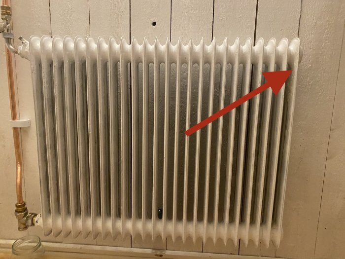En gammal vit radiator med en röd pil som pekar på toppen av radiatorens högra sida.