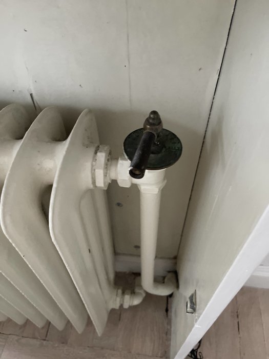 Vit radiator med termostatvred på max och synliga rör mot en vägg.