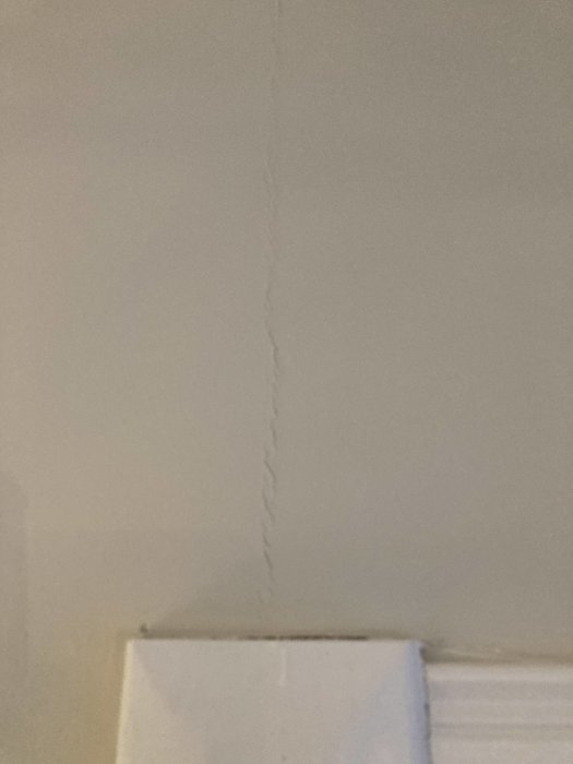 Renoverad vägg med en synlig spricka ovanför vit snickeri efter nyligen genomförd målning.