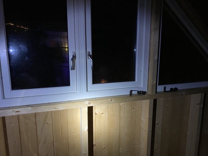 Nytt fönsterparti installerat i trävägg, taget nattetid med synlig inomhusbelysning genom fönstren.