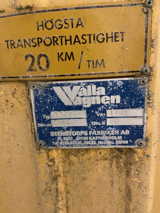 Gul sliten skylt som anger 'HÖGSTA TRANSPORTHASTIGHET 20 KM/TIM' ovanför en blå identifikationsskylt för 'Valla vagnen'.