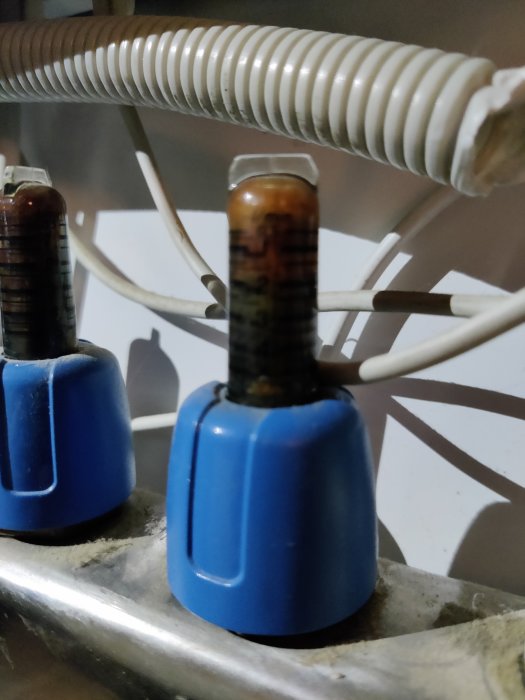 Mätglas fyllt med brunt slam i ett vattenburet värmesystem som tyder på föroreningar i systemet.