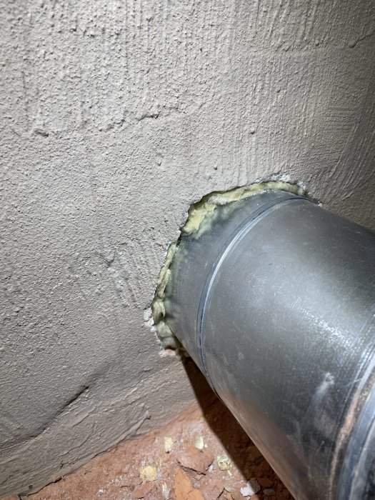 Metallrör som går igenom en vägg med isoleringsskum runt kanterna för tätning.