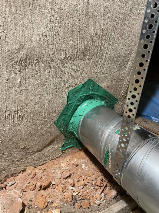 Ventilationsrör som går genom en vägg isolerat med grön tejp, på en oisolerad vind.