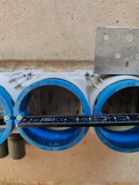 Ett måttband över två blå plastledningsrör med en monteringsplatta i bakgrunden.