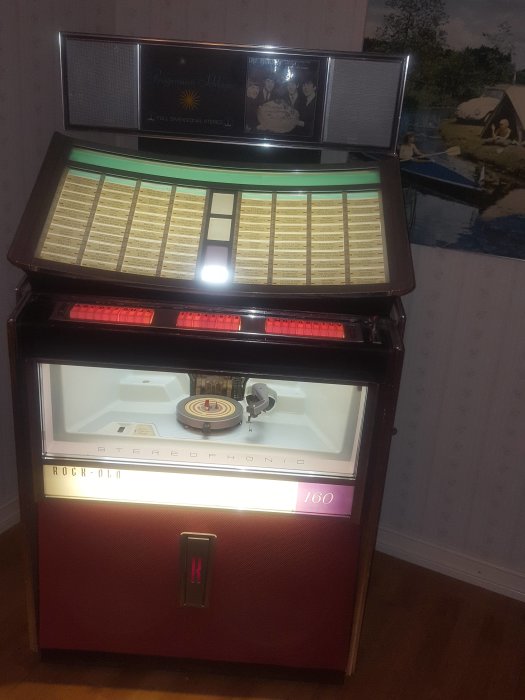 Restaurerad jukebox med tänd skärm och öppet skivfack i ett rum, klar för användning.