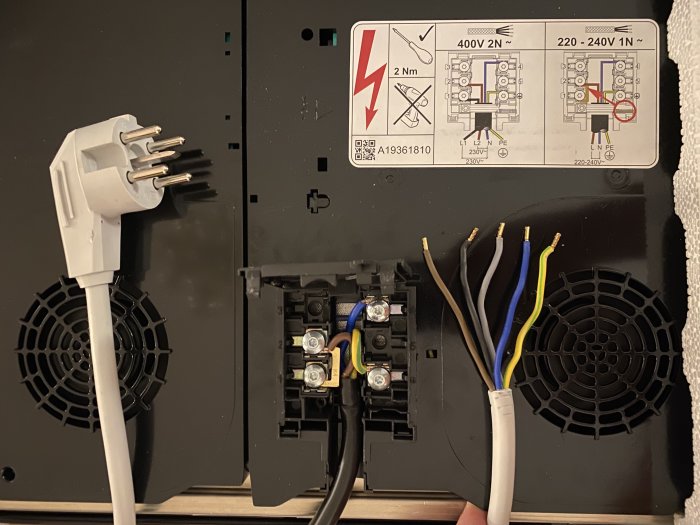 En öppen induktionshälls bakpanel med perilex-kontakt och två avskalade kablar redo för installation.