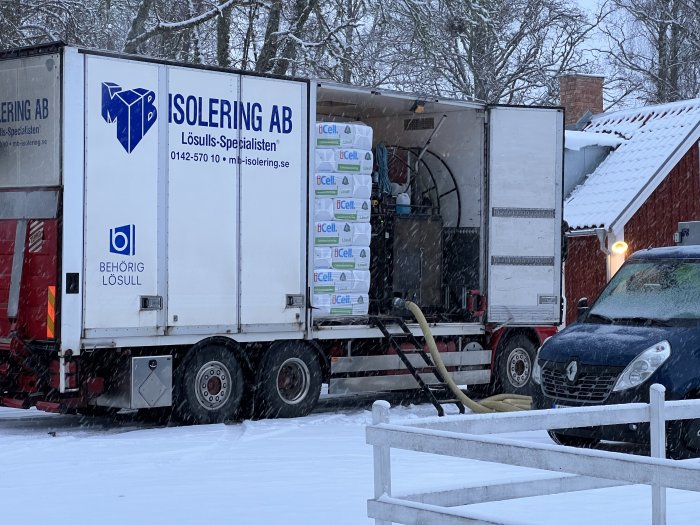 Lastbil med celulosaisolering parkerad i snöigt landskap under isoleringsarbete.