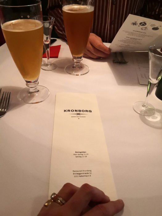 Människohänder vid bord med två öl och meny från restaurang Kronborg för danska smörrebröd.