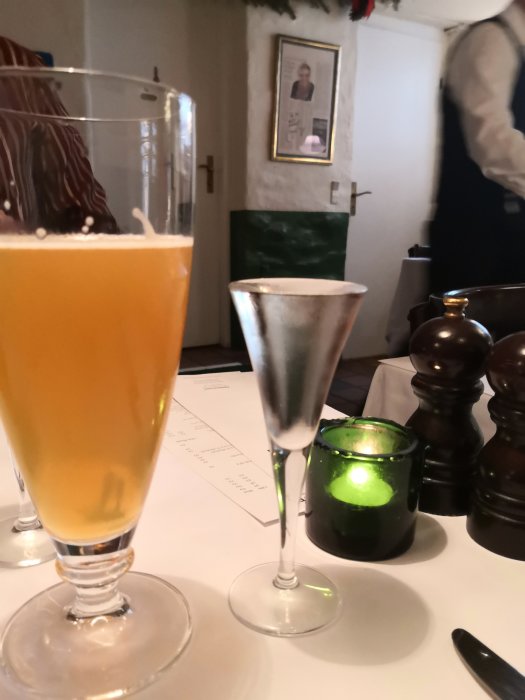 Ölglas och tom snapsglas på bord med meny i bakgrunden, inomhusmiljö på restaurang.