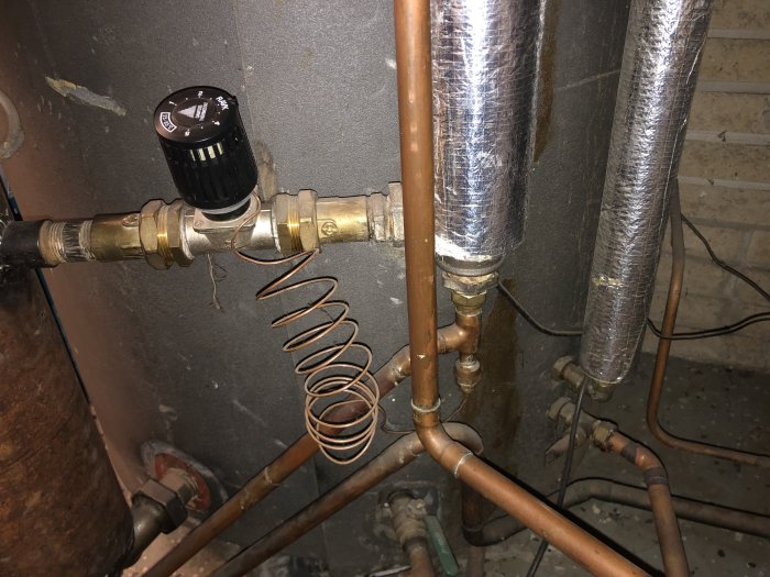 Värmesystem med kopparledningar och termostatventil monterad på rör, i en teknisk installation.
