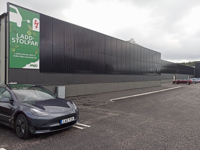 Tesla parkerad framför ICA-butik med solpaneler på väggen och skylt om laddstolpar.