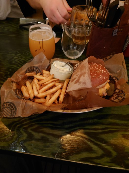 Hamburgare med pommes frites och dippsås på en träbräda, ölglas och vatten på ett barbord.