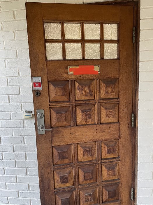 Träyterdörr med kvadratiska glasrutor längst upp, diverse låskistor och en vit tegelvägg i bakgrunden.