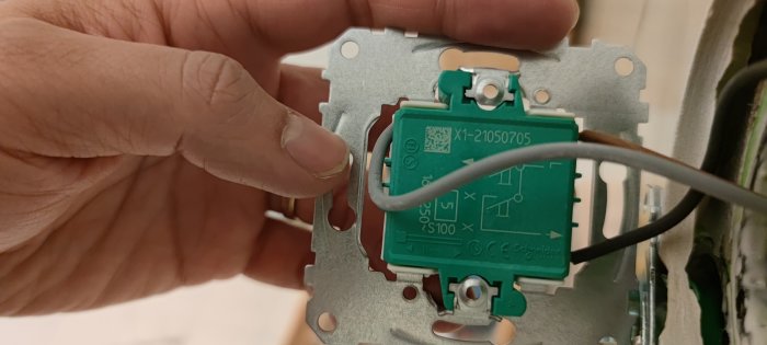 Närbild av en hand som håller en ej färdiginstallerad dimmer monterad bakom en Schneider knappsats.