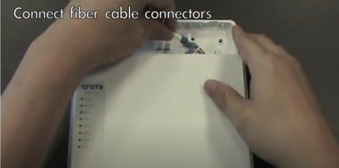 Händer ansluter fiberkabelkontakter till en vit mediaomvandlare, text "Connect fiber cable connectors".