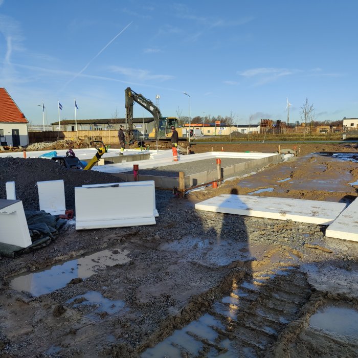 Byggarbetsplats med kantelement och cellplast installerade, arbetare och grävmaskin i bakgrunden.