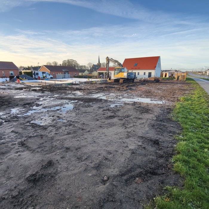 Byggarbetsplats med kantelement och cellplast, grävmaskin och hus i bakgrunden.