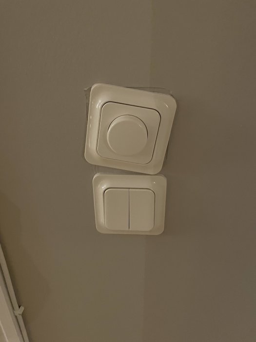 Två vita strömbrytare på vägg, en dimmer ovanför och en med två knappar nedanför.