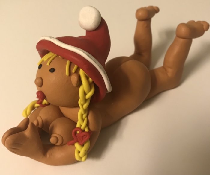 Leksaksfigur av lera som föreställer en baby med röd hatt och flätor.