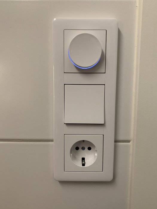 Väggmonterad elanordning med en dimmer och två brytare i linje ovanför ett vägguttag.