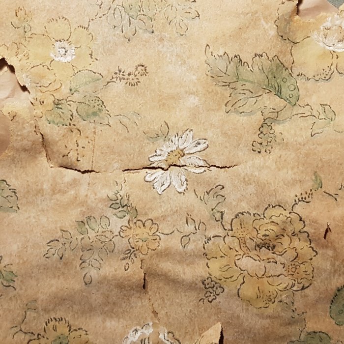 Närbild på flera lager gamla tapeter med blekt blommönster, indikerar historiska inredningsstilar.